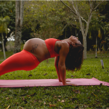 A pregnant person does a yoga pose in a park.