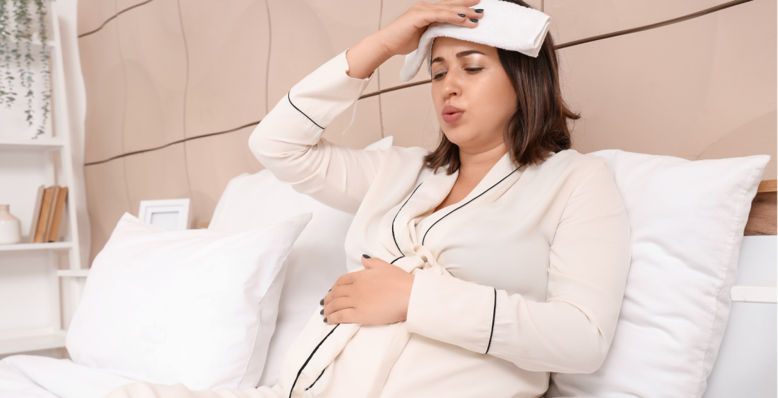 A pregnant person with a fever is sitting in bed at home.