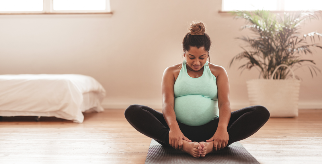 A pregnant person does yoga in a sunny room.